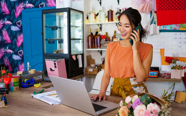 A young female flower shop owner on the phone in front of her laptop